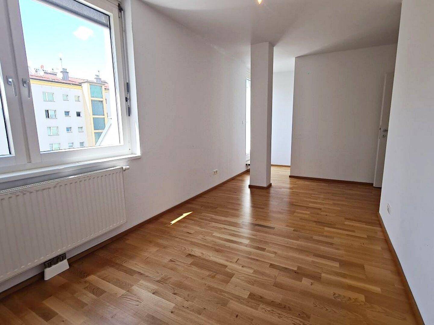 Helles Zimmer mit Parkettboden und Fensterblick auf die umliegenden Gebäude in der Stadt.