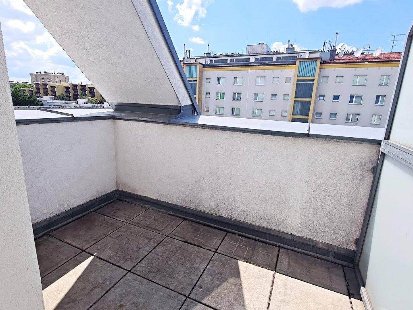 Kleiner Balkon mit Fliesenboden und Blick auf die städtische Umgebung unter blauem Himmel.