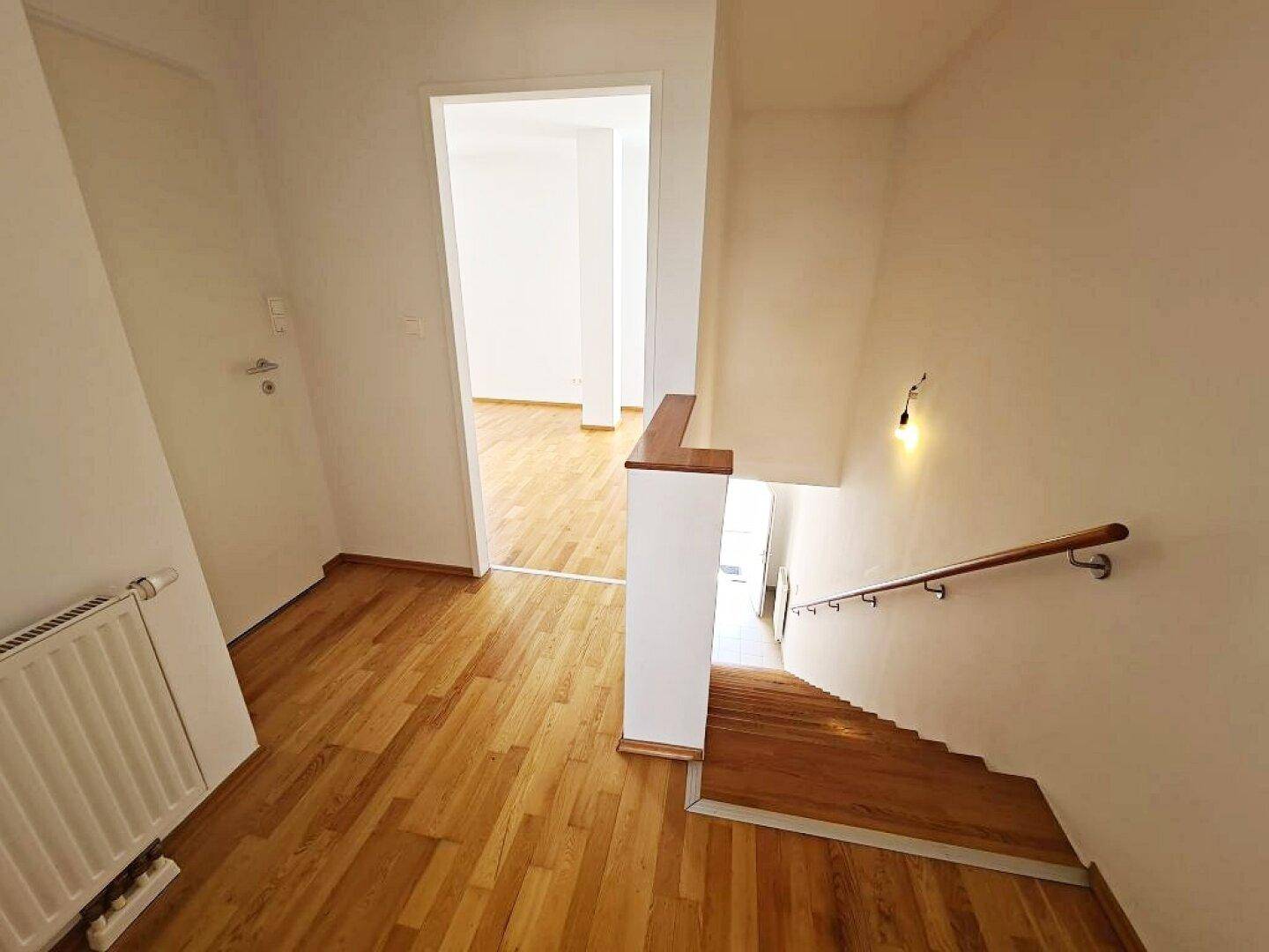 Heller Flur mit Holztreppe und Parkettboden, der zu weiteren Räumen und Ebenen führt.