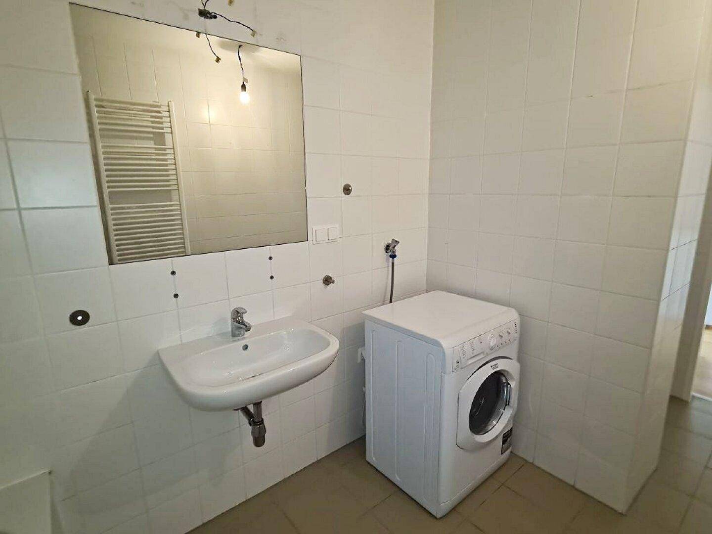 Badezimmer mit Waschbecken, Spiegel und Platz für eine Waschmaschine, praktisch und funktional.