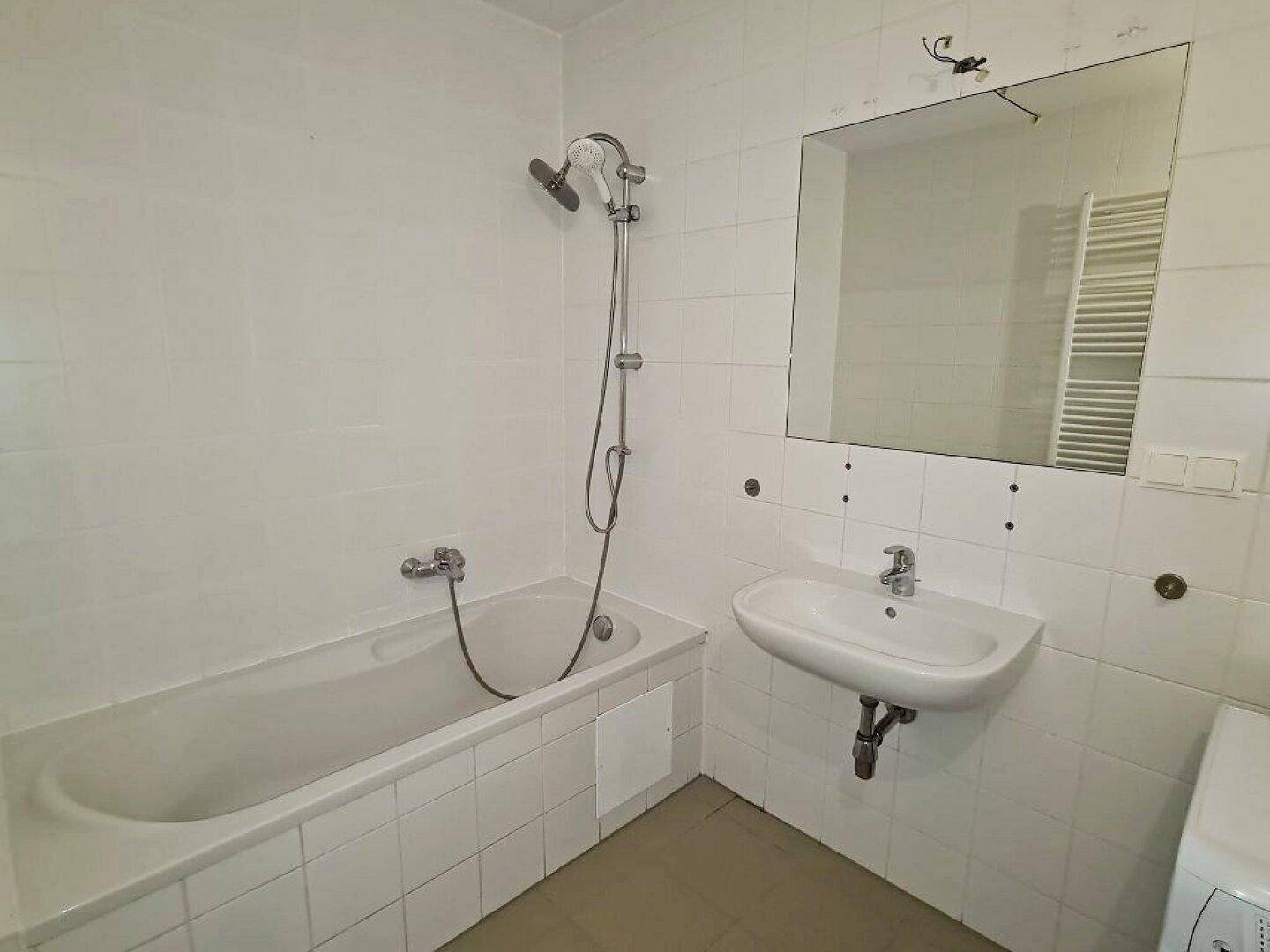 Badezimmer mit Badewanne, Duscharmatur und Waschbecken, umgeben von weißen Fliesen.