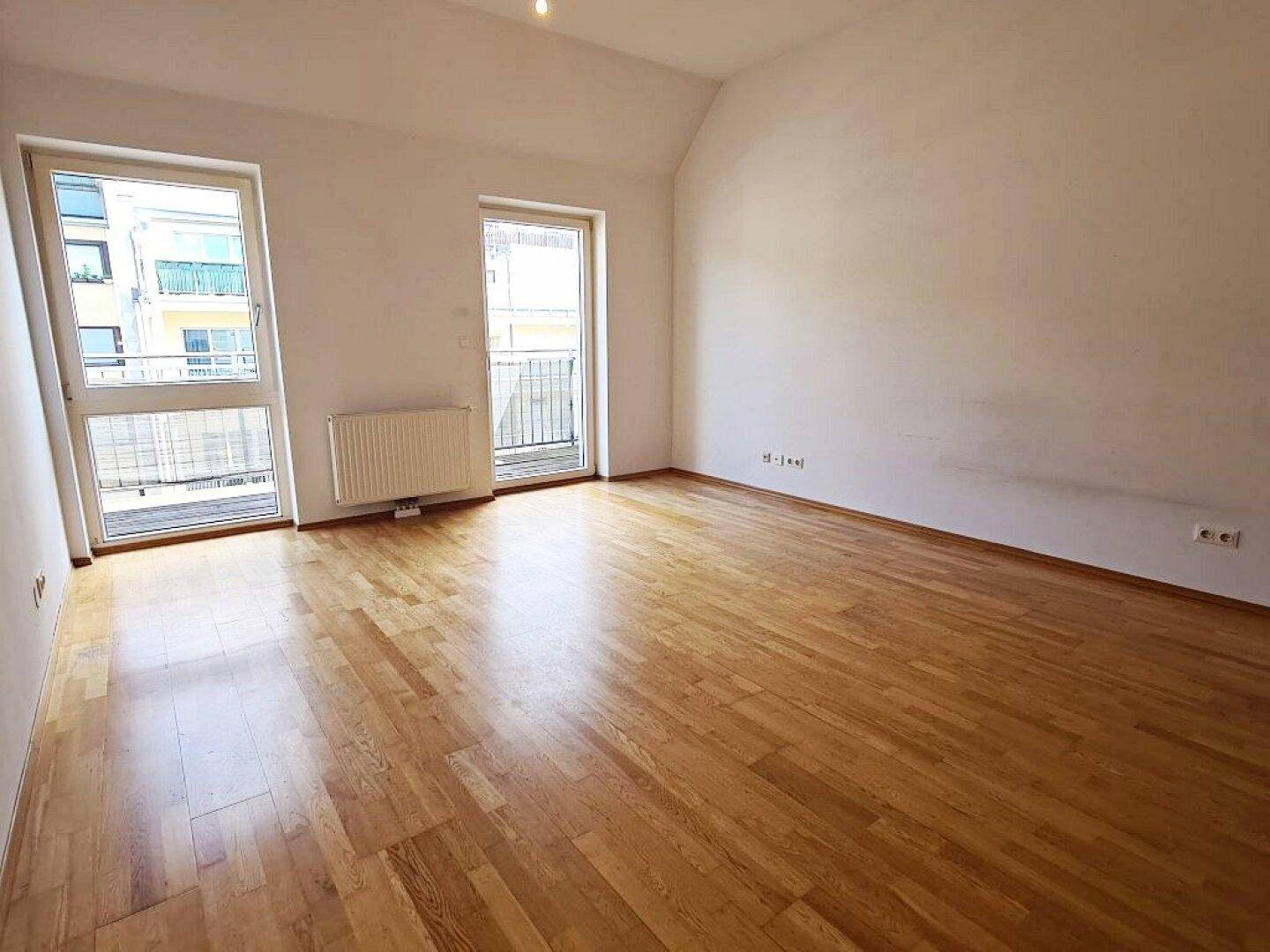 Geräumiges Zimmer mit Parkettboden und zwei Fenstern, die zu französischen Balkonen führen.
