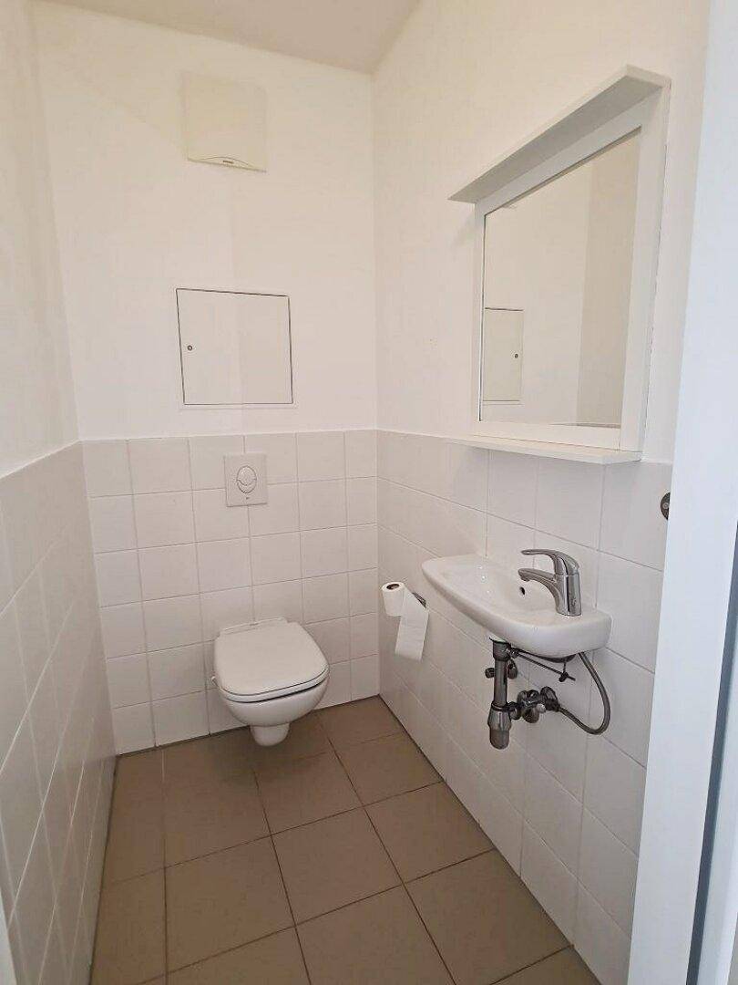 Separate Toilette mit WC, kleinem Waschbecken und weißen Wandfliesen, ideal als Gästetoilette.