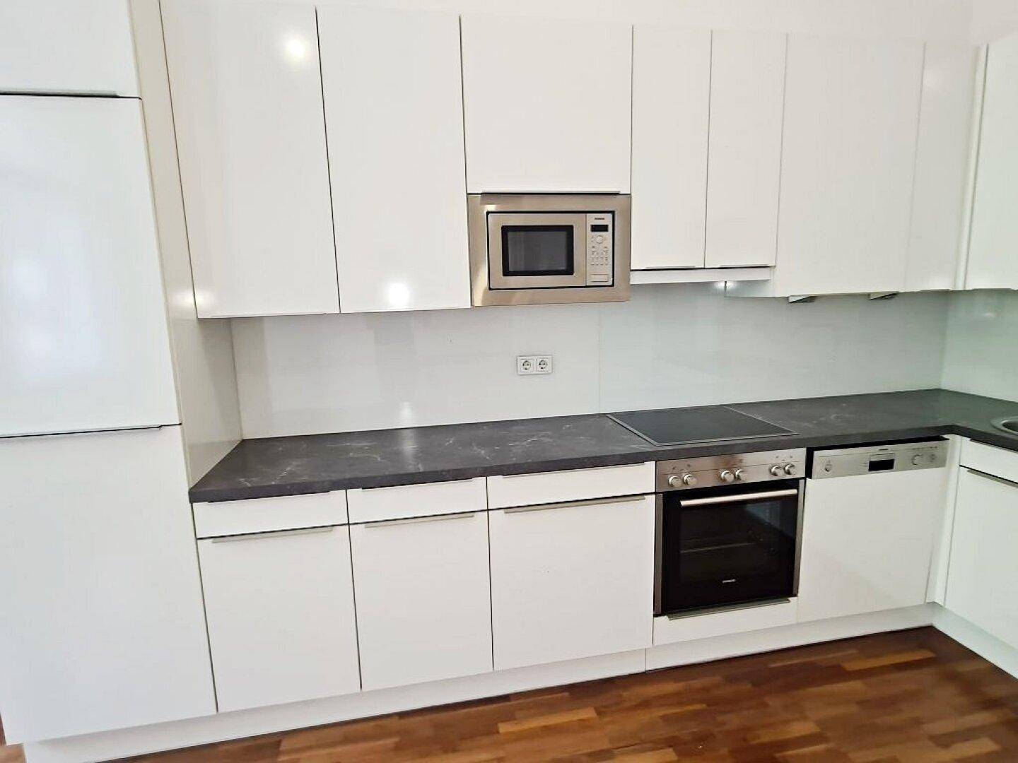 Detailansicht der modernen weißen Küche mit Mikrowelle, Backofen und Induktionskochfeld.