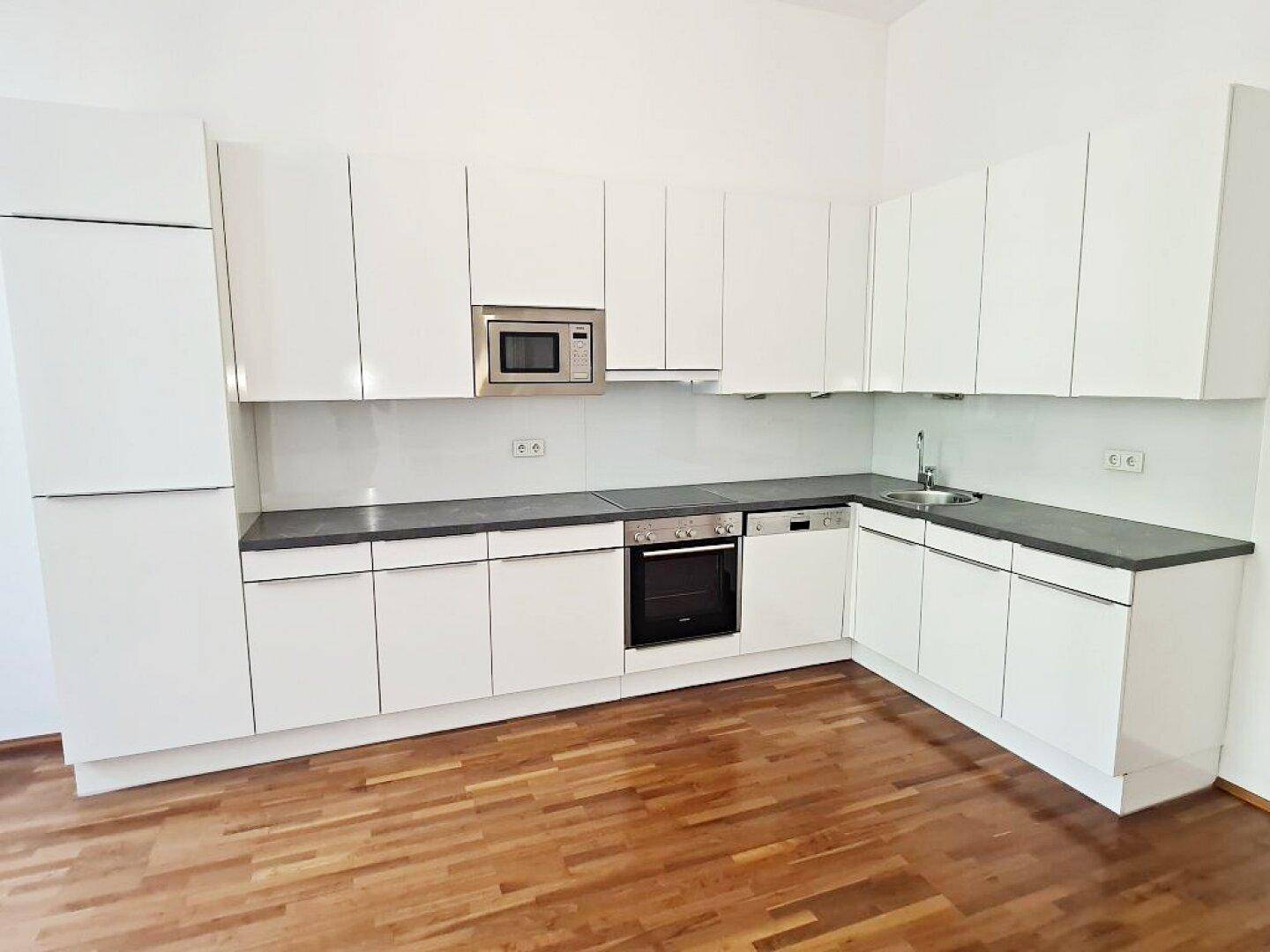 Moderne weiße Einbauküche mit dunkler Arbeitsplatte und integrierten Geräten.