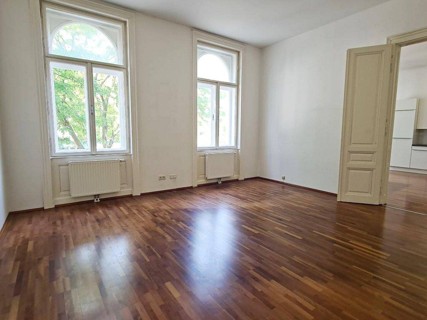 Geräumiges Zimmer mit Parkettboden und hohen Fenstern, offen zum Wohnbereich.