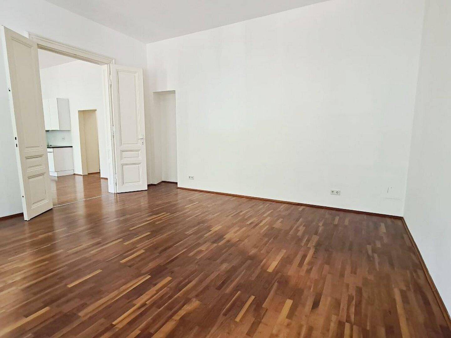Geräumiges Zimmer mit Parkettboden und weißen Wänden, mit offenem Durchgang.