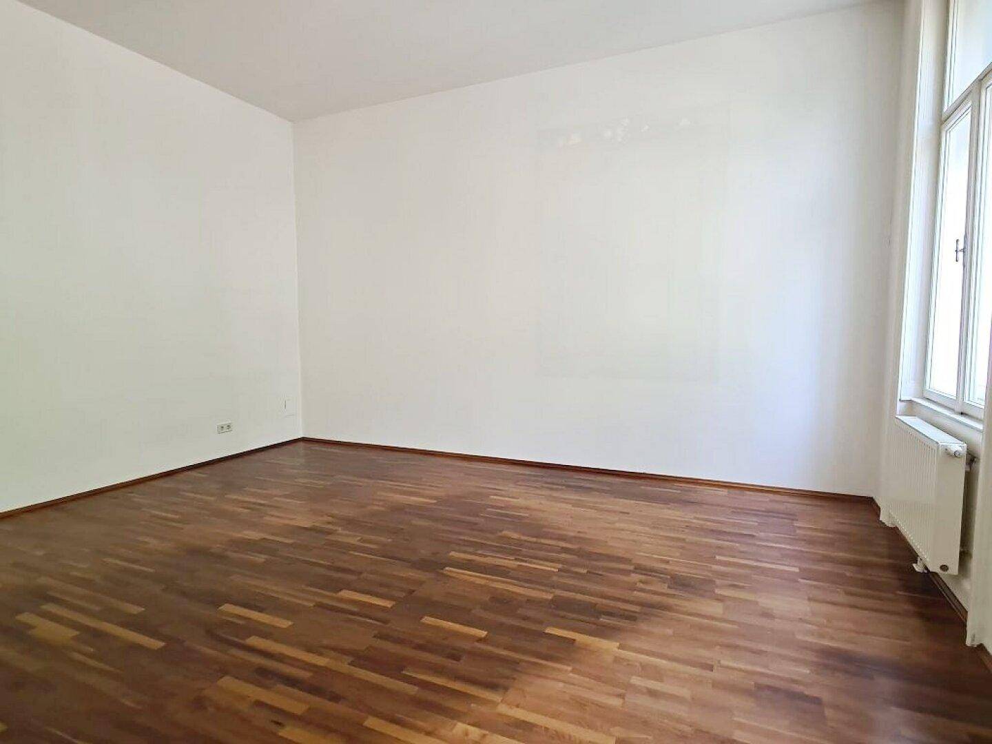 Leeres Zimmer mit Parkettboden und weißen Wänden, bereit zur individuellen Gestaltung.
