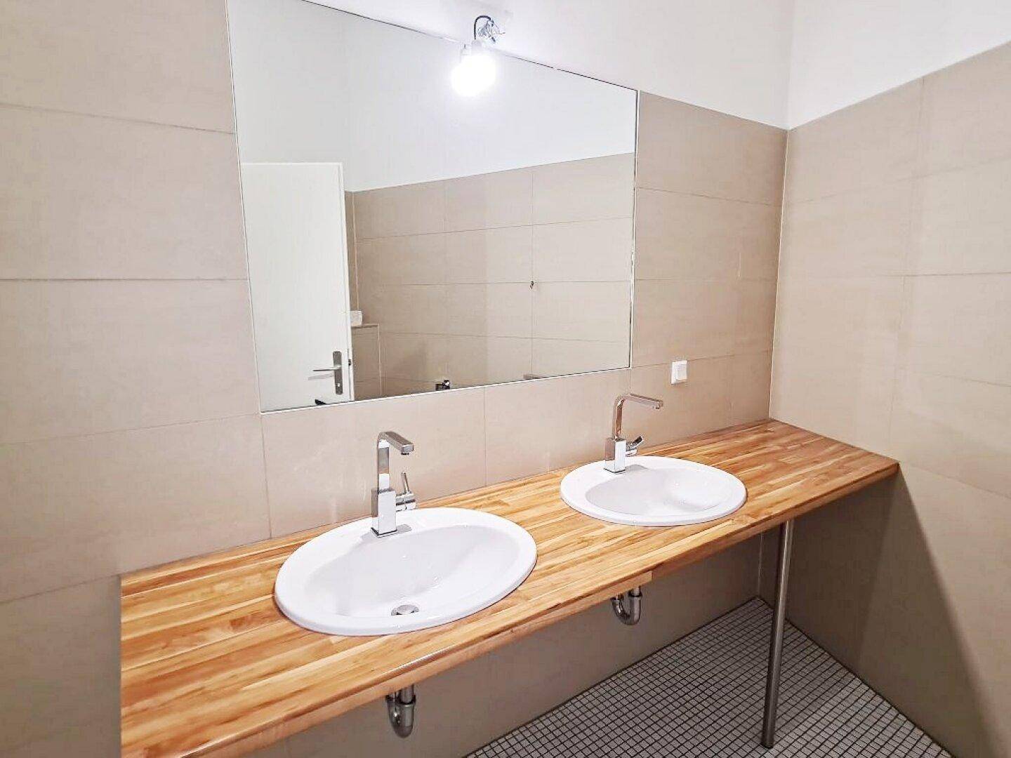 Modernes Badezimmer mit Doppelwaschbecken auf Holzplatte und großem Spiegel.