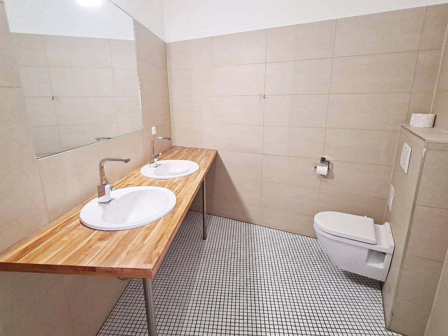Modernes Badezimmer mit Doppelwaschbecken, wandhängendem WC und hellen Fliesen.
