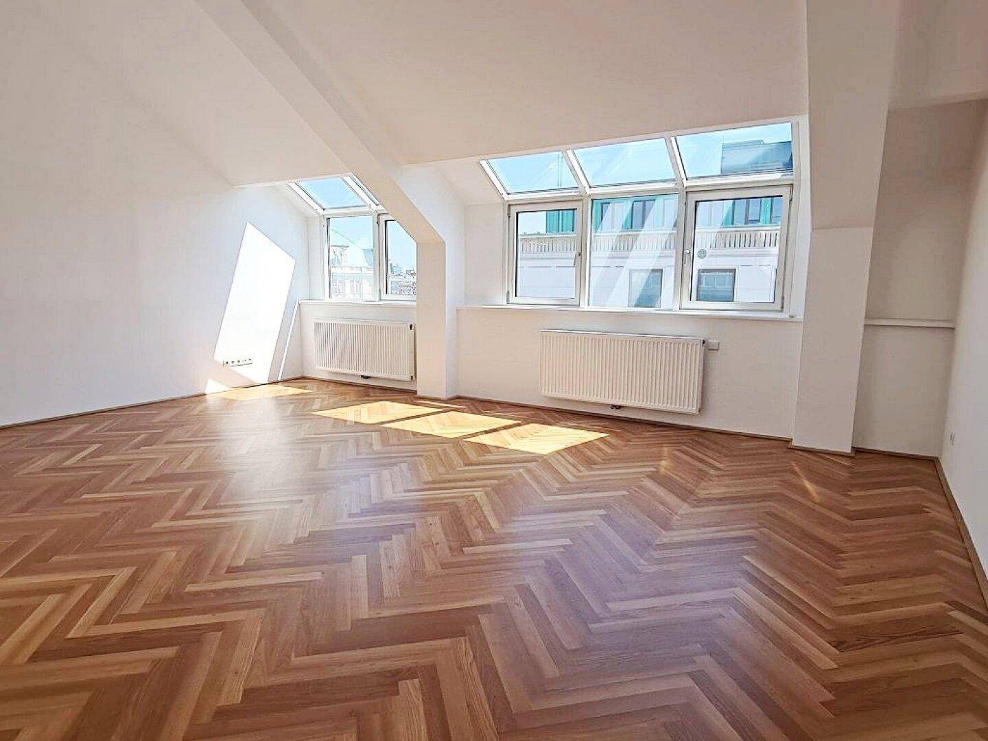 Helles Zimmer mit Fischgrätparkett und großen Dachfenstern, ideal als Wohn- oder Schlafzimmer.