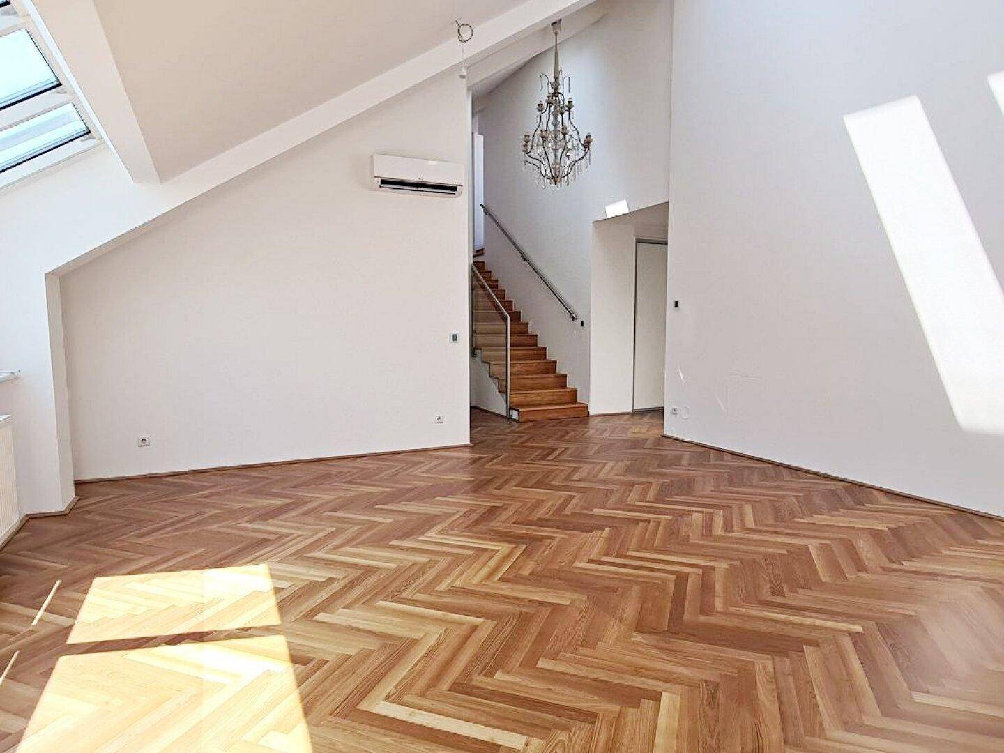 Geräumiger Wohnbereich mit Fischgrätparkett, Treppe und Klimaanlage, lichtdurchflutet.