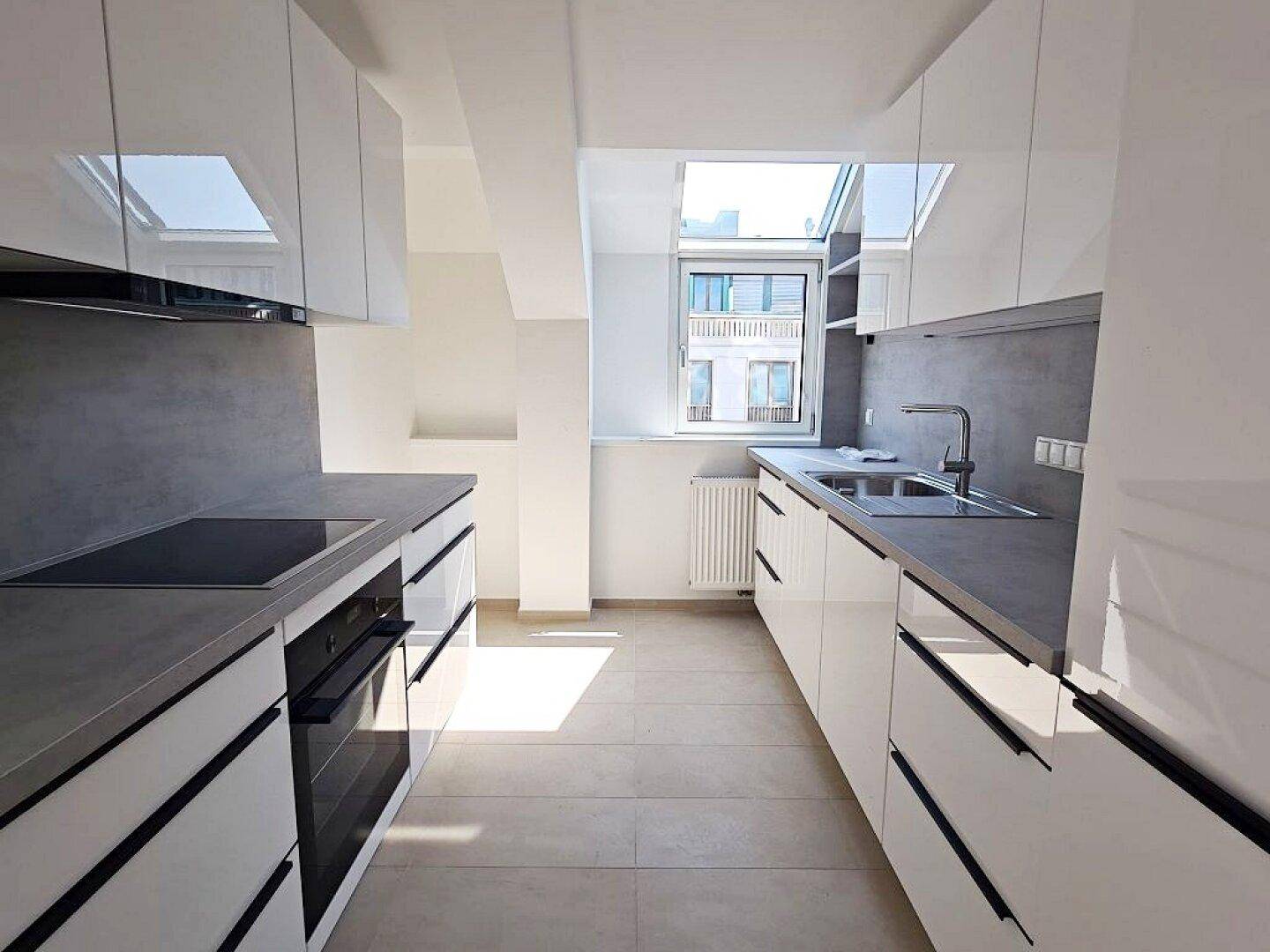 Moderne Küche mit weißen Hochglanzfronten, grauer Arbeitsplatte und integrierten Geräten.