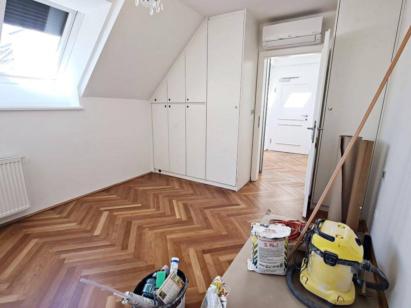 Schlafzimmer mit schrägen Wänden, integrierten Schränken und Zugang zu weiteren Räumen.