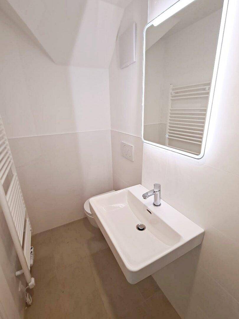 Helles WC mit wandhängender Toilette, modernem Waschbecken und beheiztem Handtuchhalter.