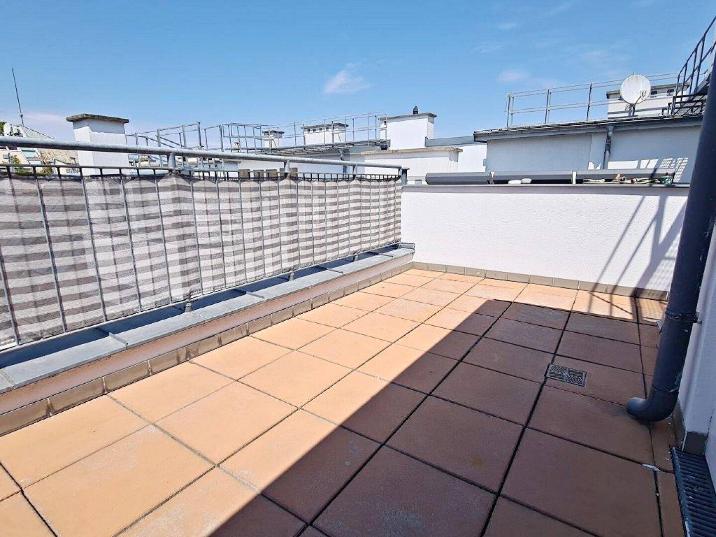 Sonnige Dachterrasse mit Fliesenboden und einem Sichtschutz am Geländer für Privatsphäre.