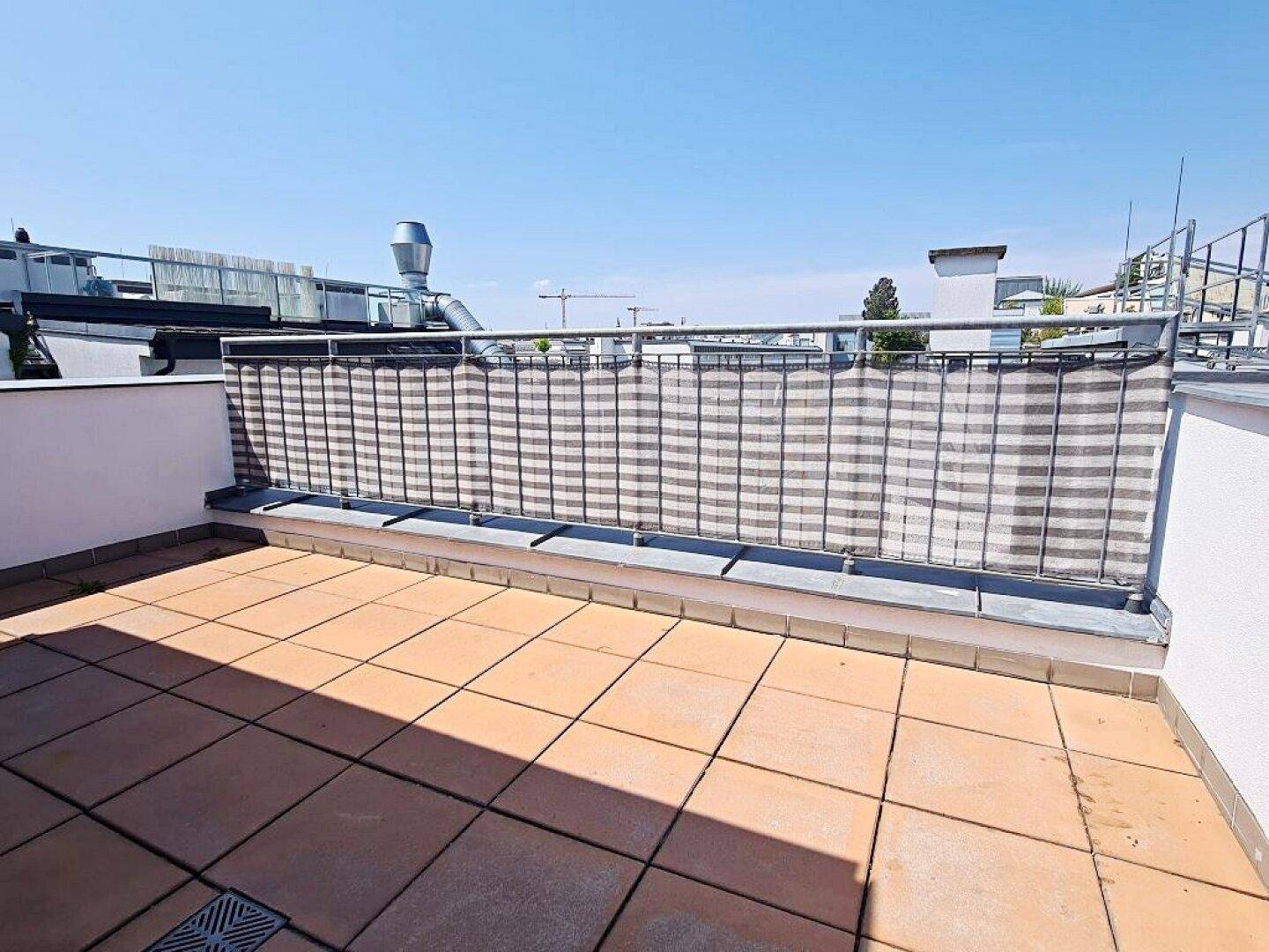 Weitläufige Dachterrasse mit Sichtschutz am Geländer und einem Panoramablick über die Stadt.