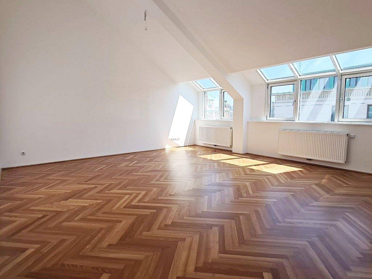 Geräumiger Wohnbereich mit hellem Fischgrätparkett, Dachschrägen und großen Fenstern für viel Licht.