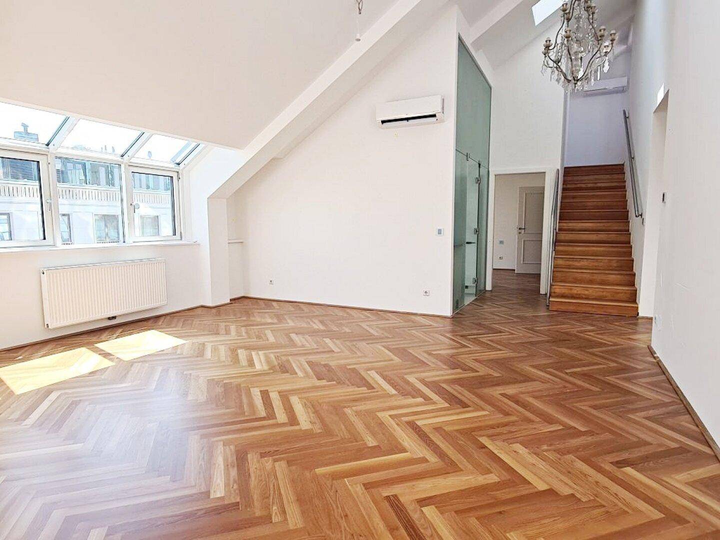 Offener Wohnbereich mit Fischgrätparkett, Treppe und Kronleuchter, der zu weiteren Räumen führt.