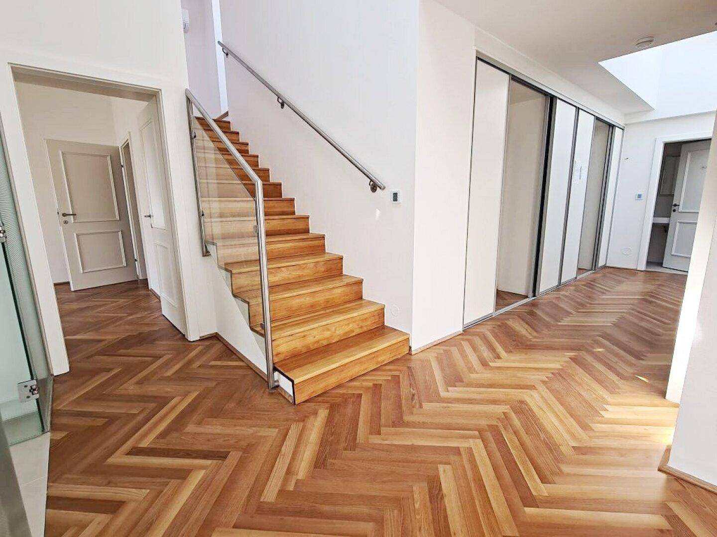 Moderner Flur mit Fischgrätparkett, Holztreppe mit Glasgeländer und Schiebetüren.
