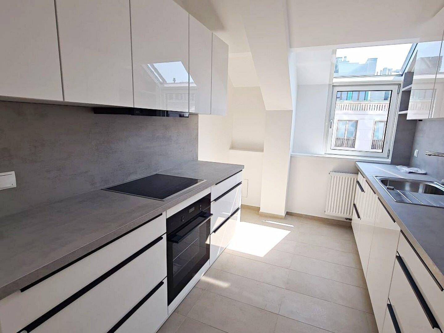 Moderne Küche mit weißen Hochglanzschränken, grauer Arbeitsplatte und integriertem Backofen.