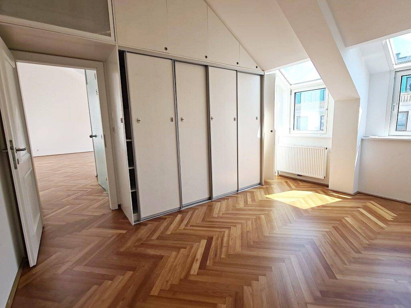 Schlafzimmer mit Fischgrätparkett, Einbauschränken und Dachfenstern, die viel Licht spenden.
