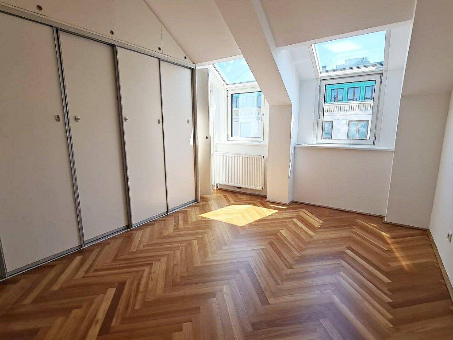 Schlafzimmer mit Fischgrätparkett, Einbauschränken und Dachfenstern, die viel Licht spenden.