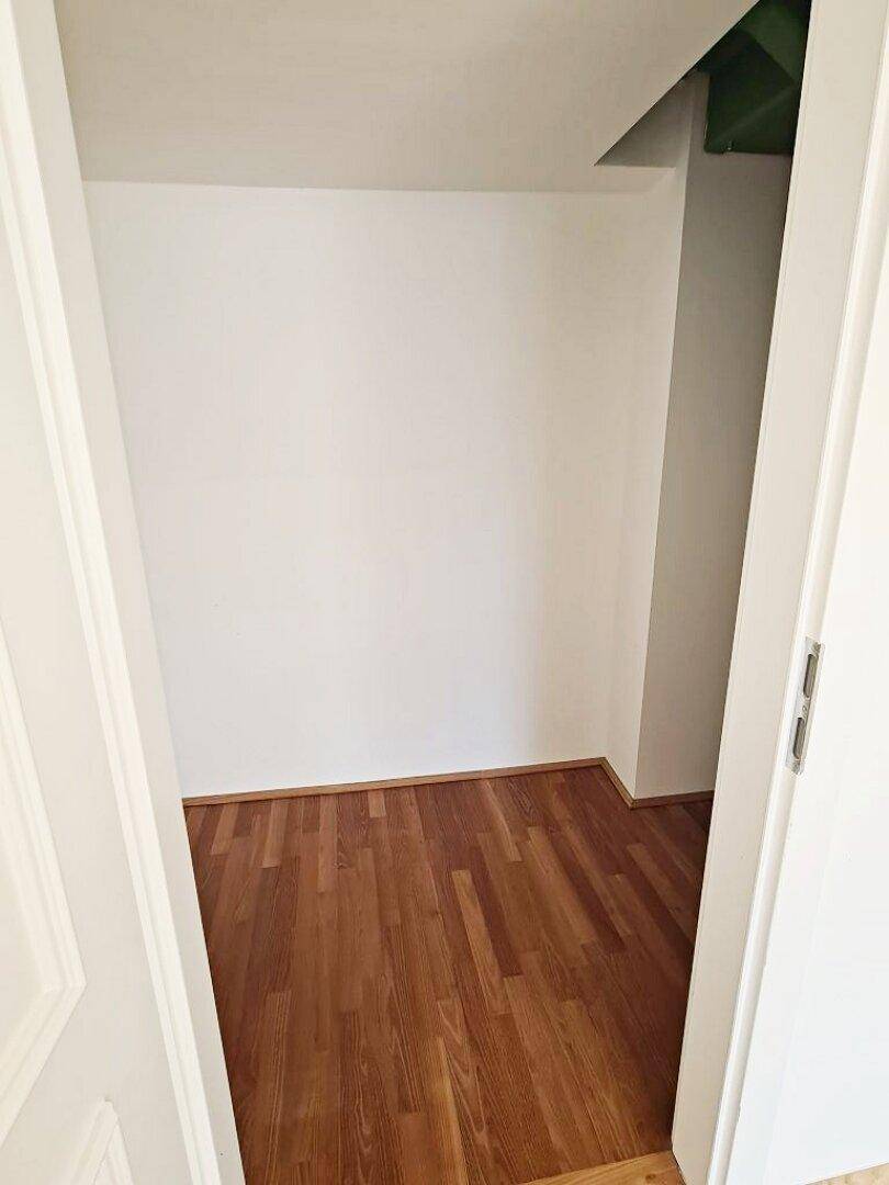 Kleiner begehbarer Kleiderschrank mit Holzboden und weißen Wänden, bereit zur Einrichtung.