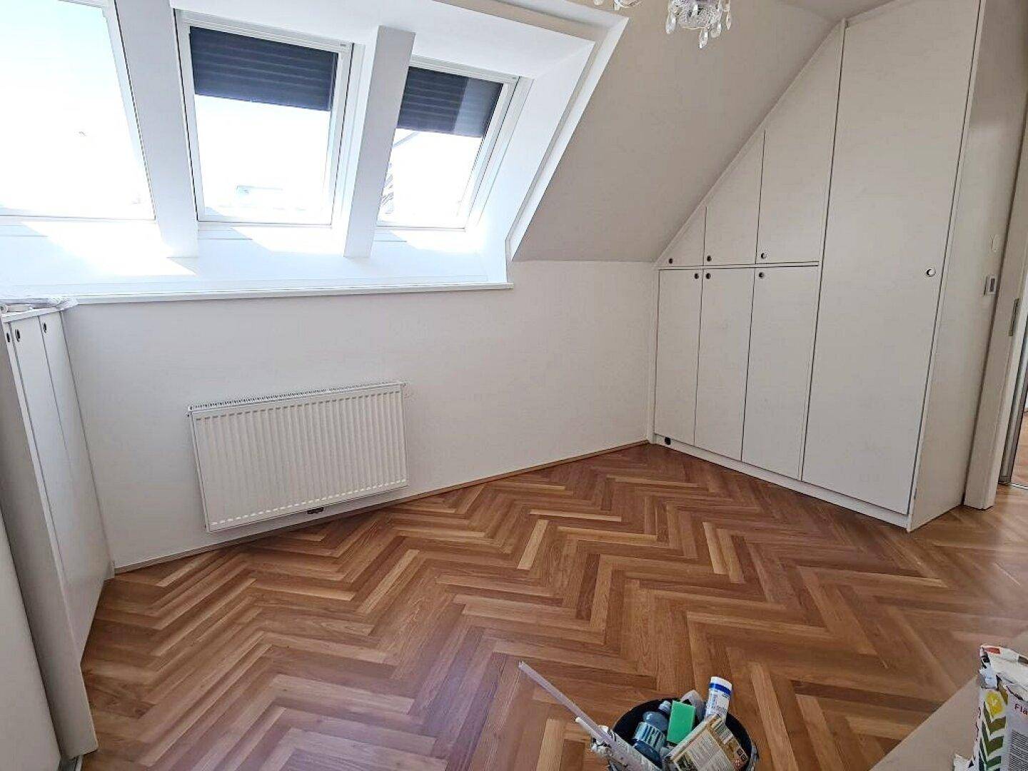 Helles Dachgeschosszimmer mit zwei Dachfenstern, Fischgrätparkett und praktischen Einbauschränken.