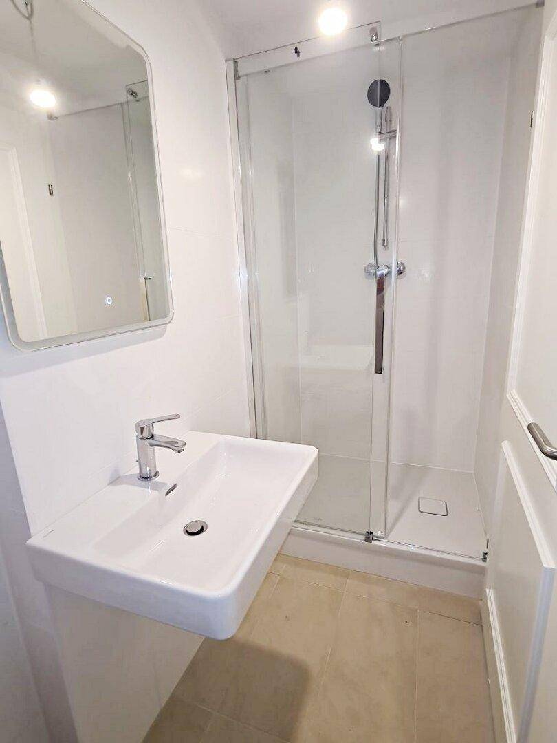 Modernes Badezimmer mit wandhängendem Waschbecken, beleuchtetem Spiegel und geräumiger Duschkabine.