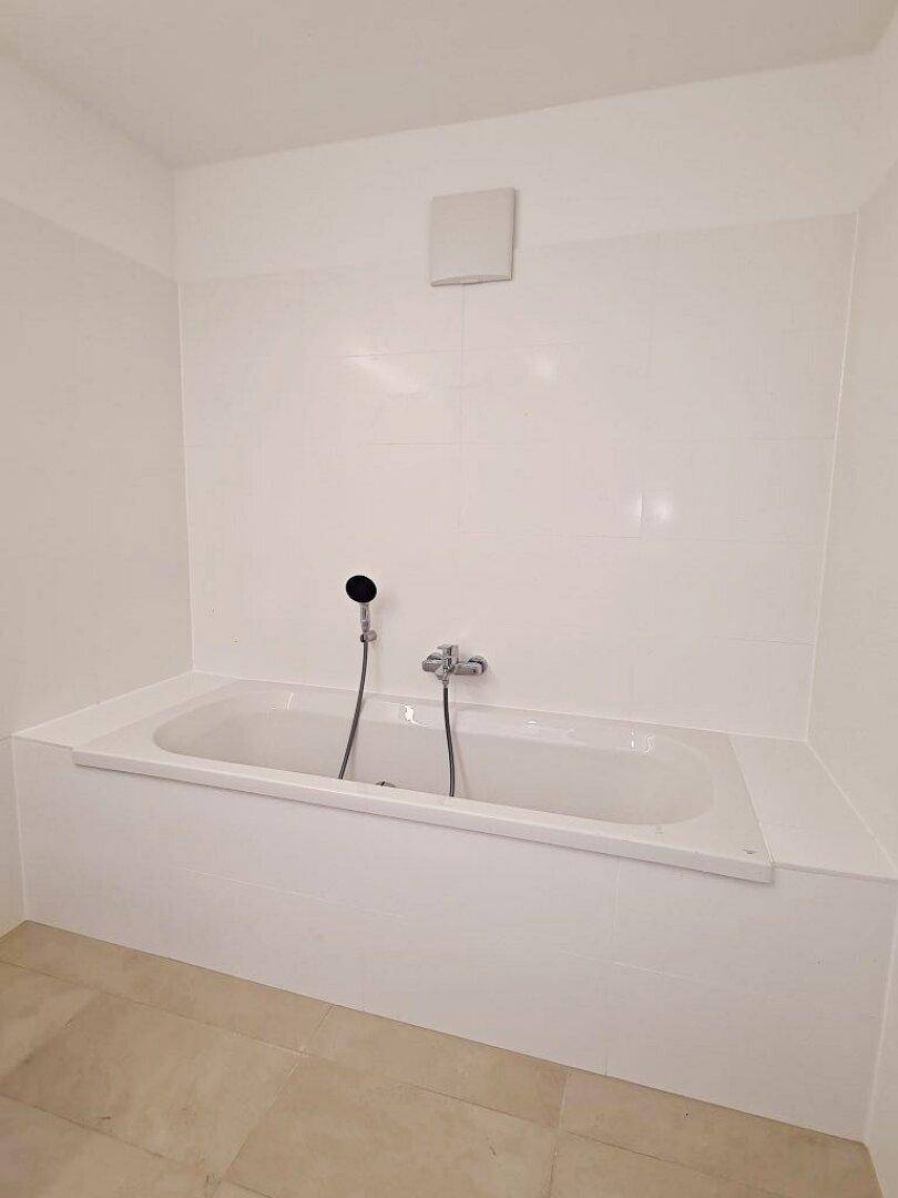 Eingebaute Badewanne mit Duscharmatur in einem minimalistischen, hell gefliesten Badezimmer.