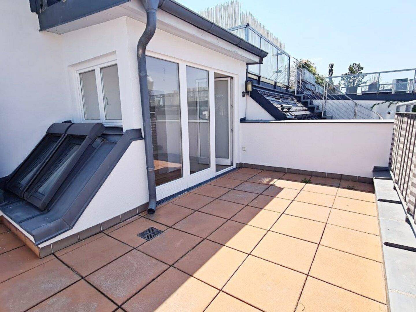 Helle Dachterrasse mit Fliesenboden und direktem Zugang zu den Wohnräumen, umgeben von weißer Fassade.