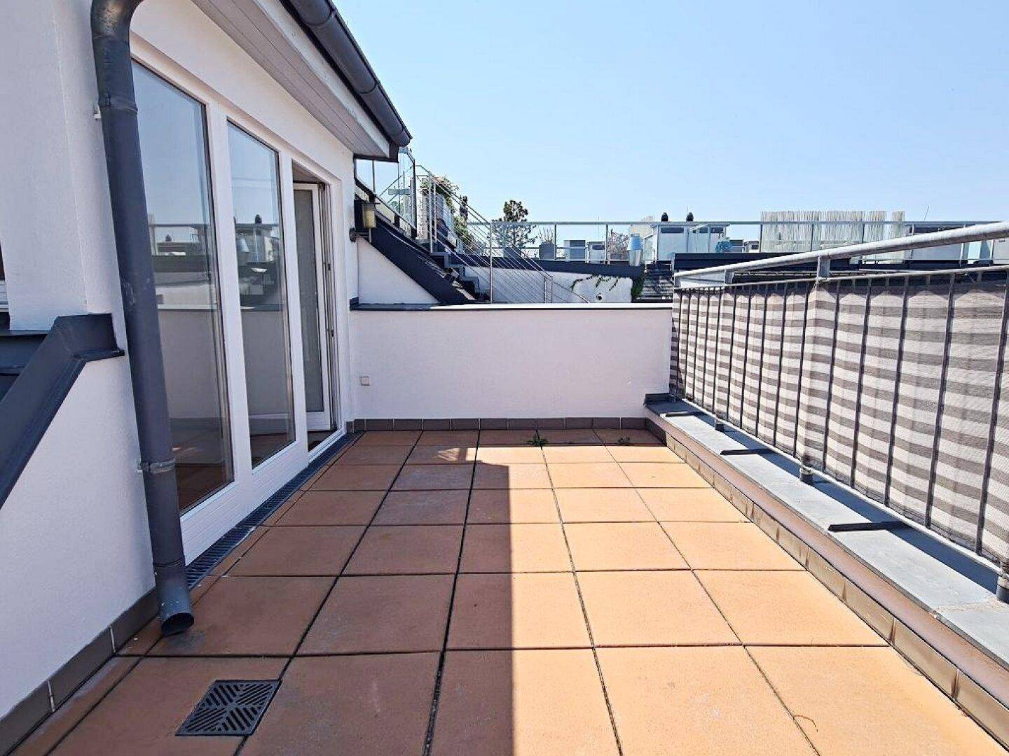Sonnige Dachterrasse mit Fliesenboden und großen Glastüren, die viel Licht in die Innenräume lassen.