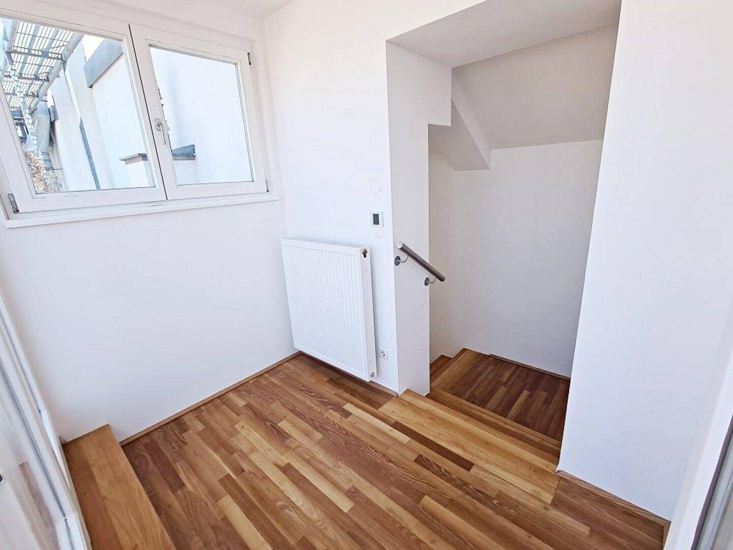 Heller Treppenbereich mit Holzstufen, Fenster und Heizkörper, führt in die untere Etage.