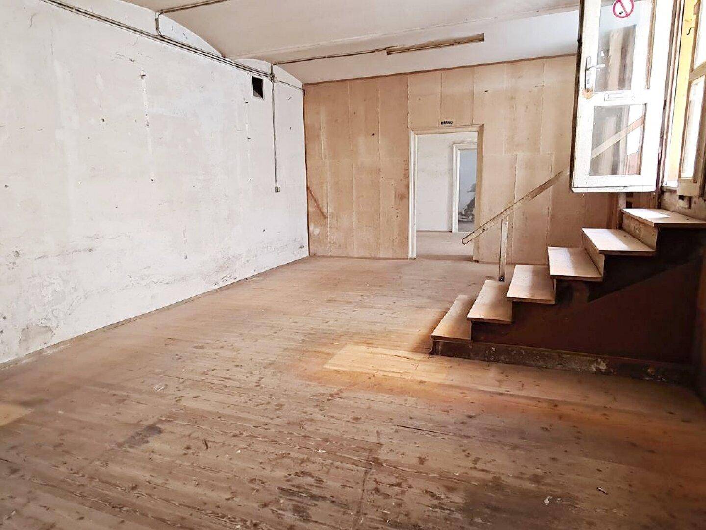 Weiterer Blick in den großen, leeren Raum mit abgenutzten Holzdielen und teilweise freigelegten Wänden.