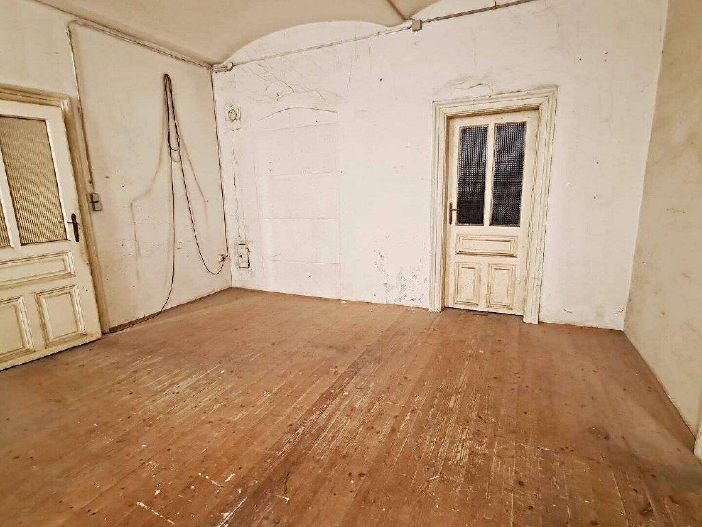 Leerer Raum mit Holzdielenboden, zwei weißen Türen mit Glaseinsätzen und einer gewölbten Decke.