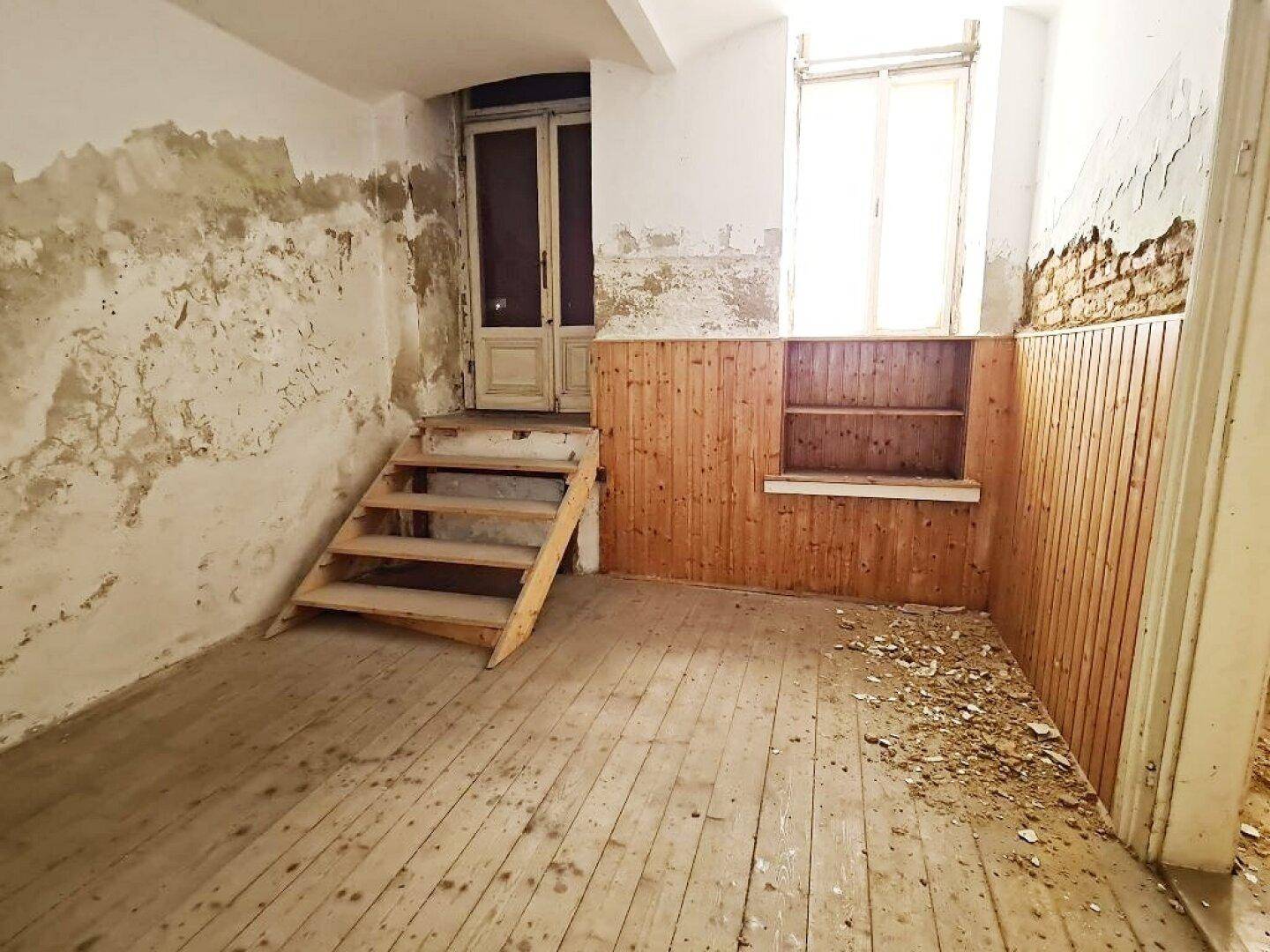 Leerer Raum mit Holzdielenboden, einer kleinen Holztreppe, einer Tür mit Glaseinsätzen und Holzvertäfelung.