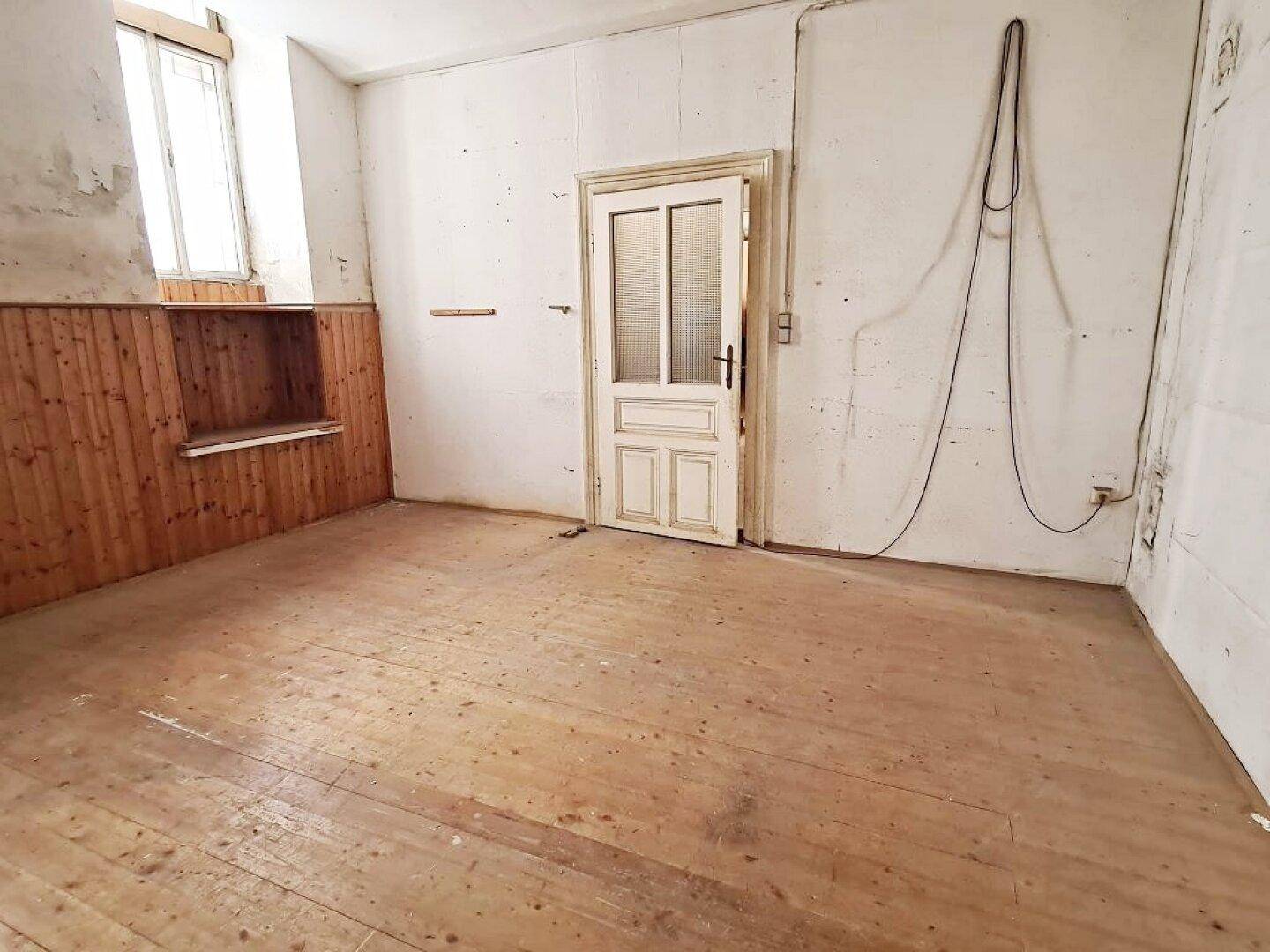 Leerer Raum mit Holzdielenboden, einer weißen Tür mit Glaseinsätzen und einem Fenster für natürliches Licht.