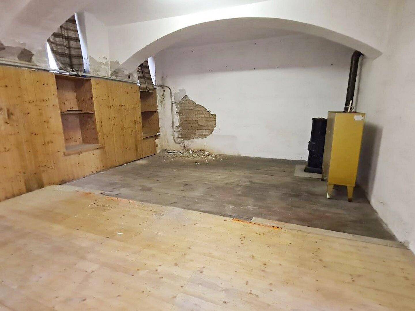 Kellerraum mit gemischtem Bodenbelag, einem gelben Ofen, Holzregalen und einer gewölbten Decke.