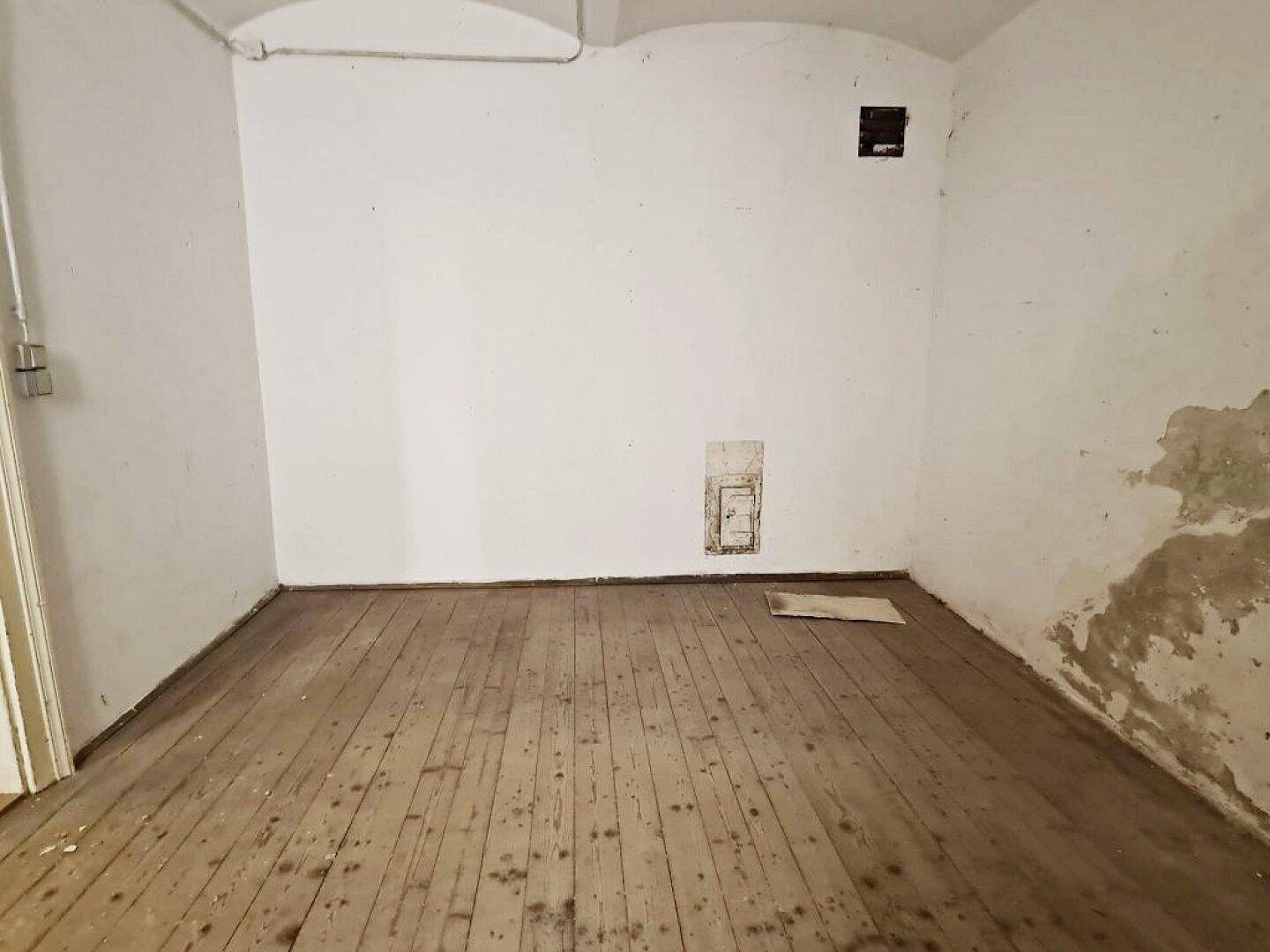 Leerer Raum mit Holzdielenboden, weißen Wänden und einer kleinen Nische, unter einer gewölbten Decke.
