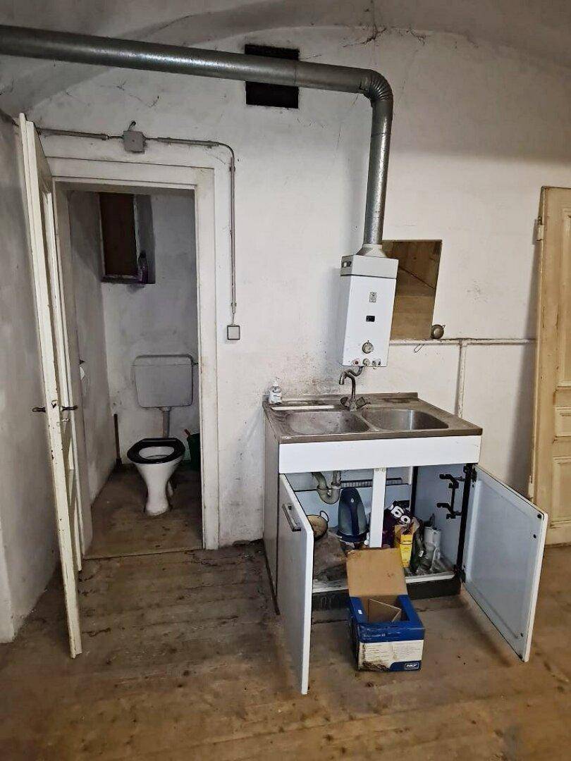 Kleiner Toilettenraum mit einfacher Toilette und einem Spülbecken mit Warmwasserbereiter.