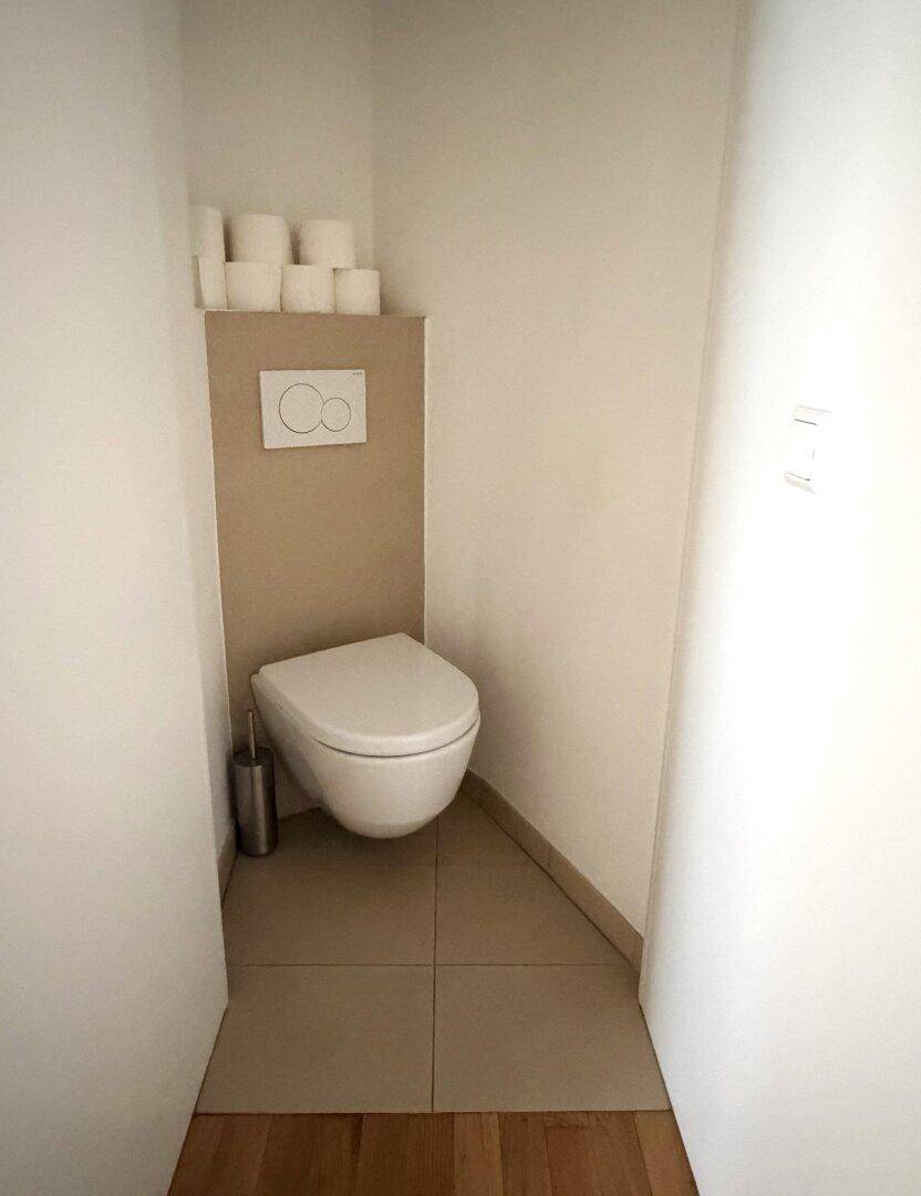 Kleines Gäste-WC mit wandhängender Toilette, moderner Spülplatte und beigefarbenen Fliesen.