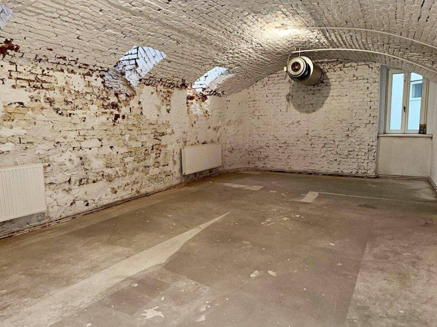 Heller Kellerraum mit gewölbter Ziegeldecke, Heizkörper und einem Fenster, das Tageslicht hereinlässt.