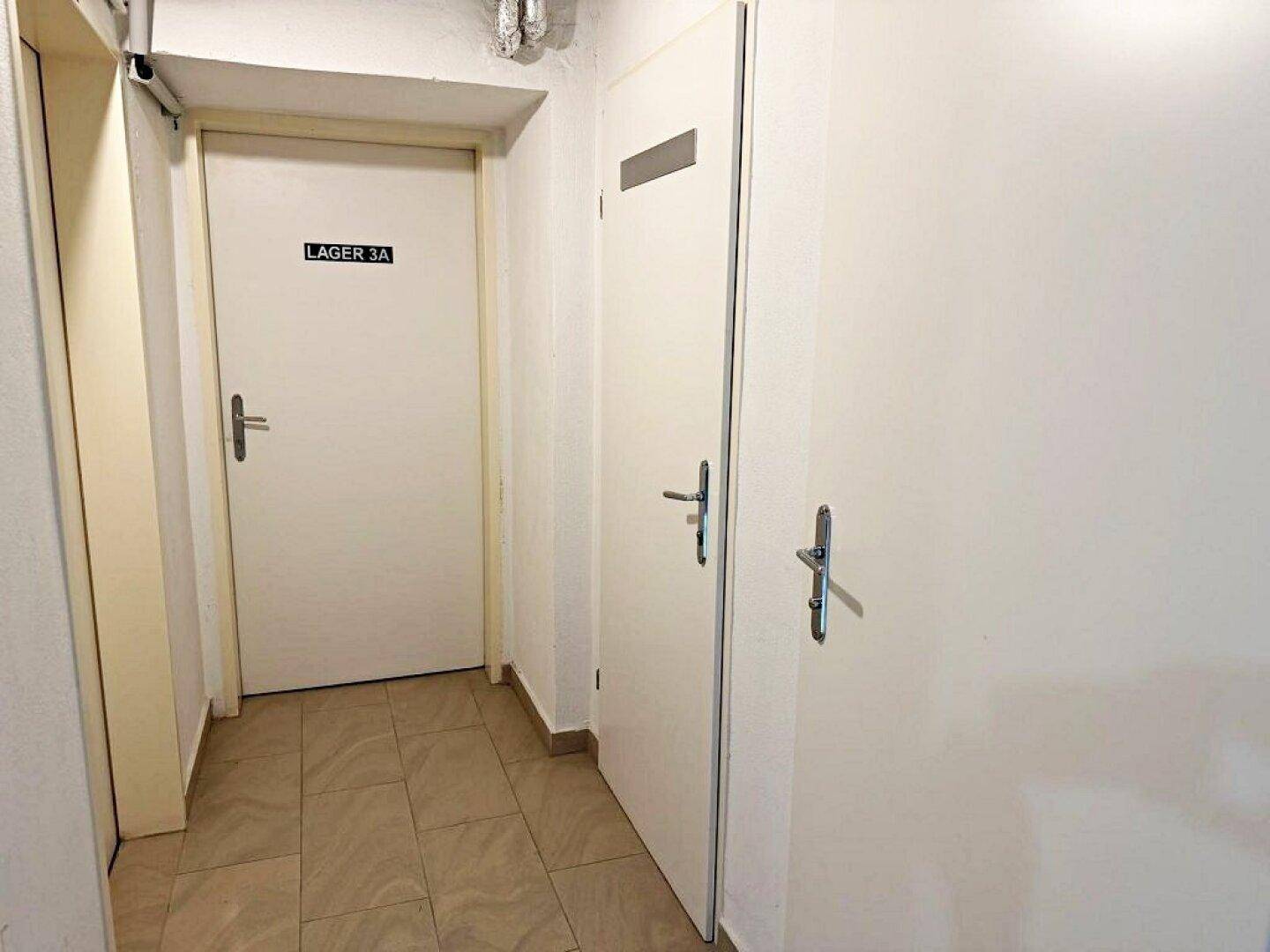 Heller Flur mit mehreren weißen Türen und einem gefliesten Boden, der zu verschiedenen Lagerräumen führt.