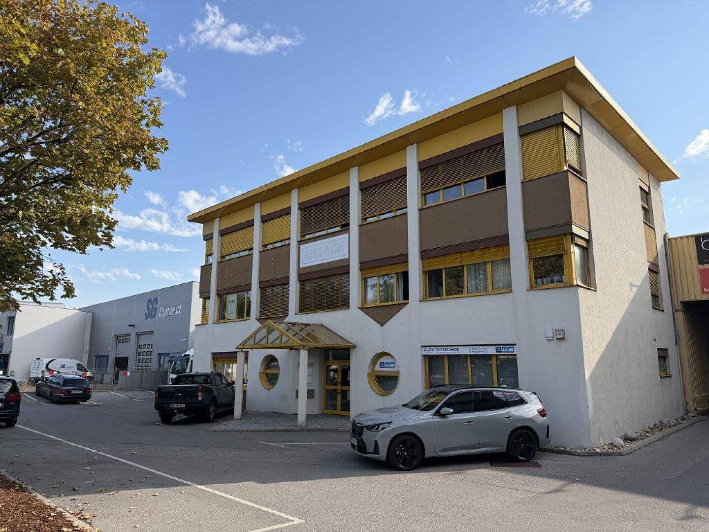 Modernes Geschäftsgebäude mit gelben Akzenten und Parkplätzen vor dem Eingangsbereich.