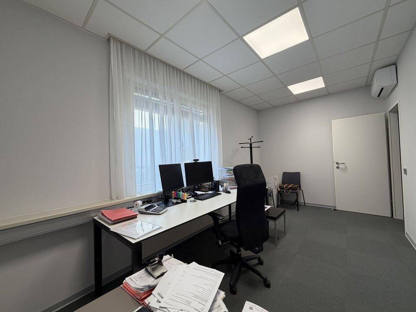 Büroarbeitsplatz mit zwei Monitoren, Teppichboden und einem Klimagerät an der Wand.