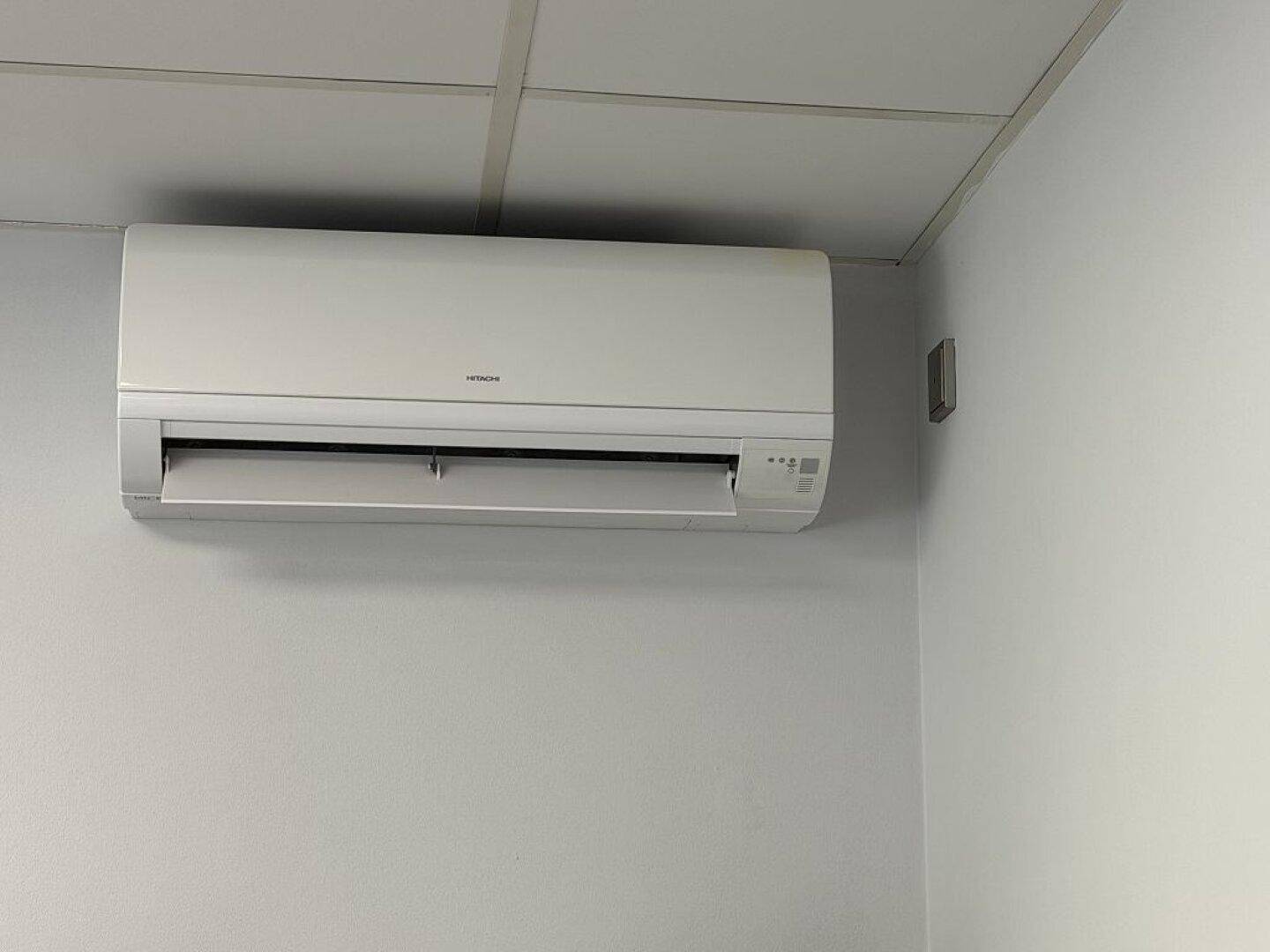Nahaufnahme einer Klimaanlage an der Wand eines Büroraums mit abgehängter Decke.