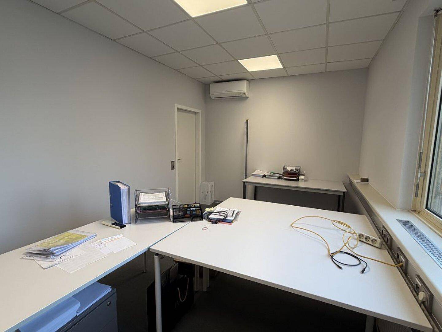 Helles Büro mit Schreibtischen, Klimaanlage und einem Fenster, das für natürliche Belüftung sorgt.