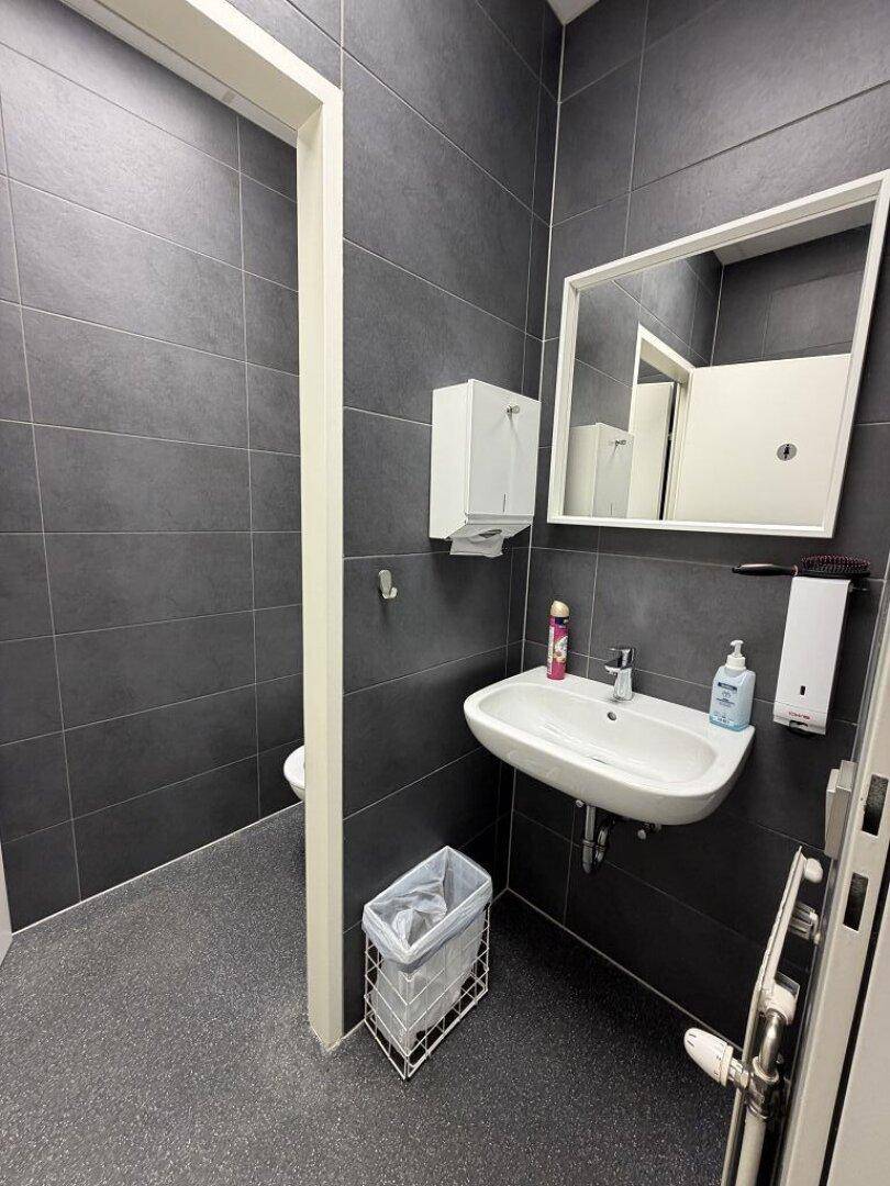 Modernes WC mit dunkelgrauen Fliesen, weißem Waschbecken und einem Spiegel.