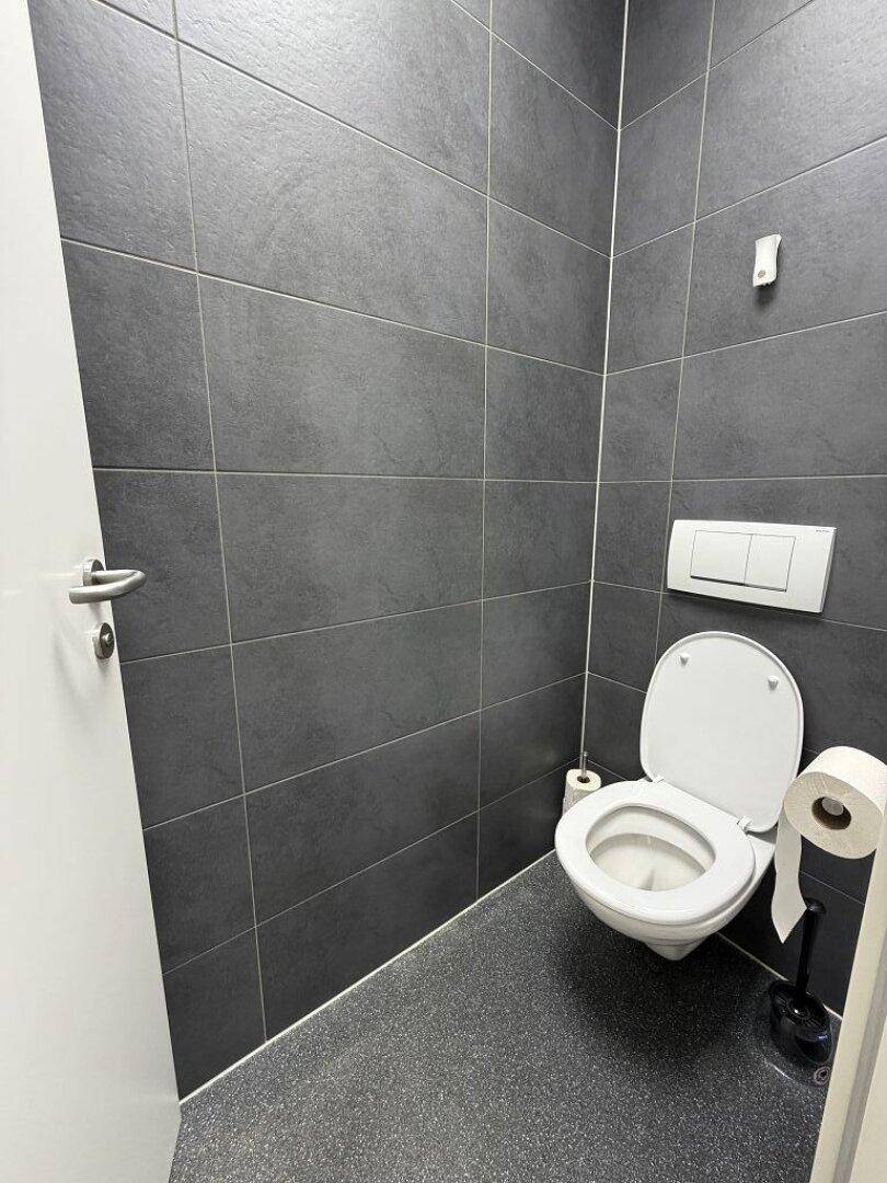 Modernes WC mit dunkelgrauen Fliesen und einer wandhängenden Toilette.